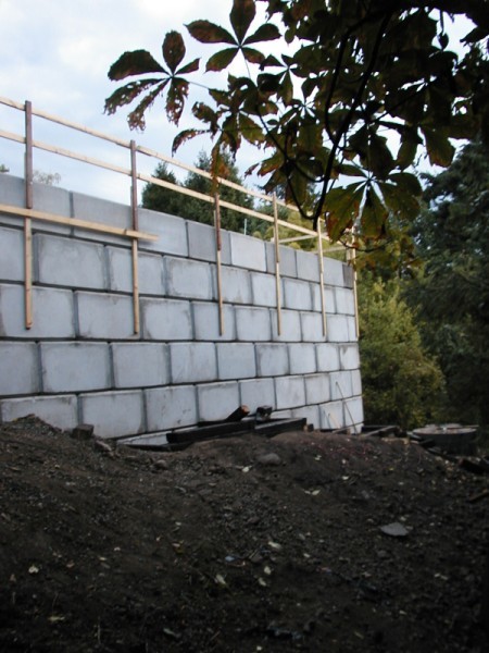Lock block retaining wall built in stepped courses against a cut slope, with timber guard rail along the top.