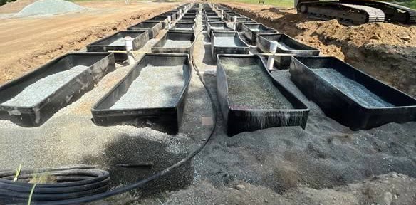 Rows of black Glendon Biofilter basins filled with media, laid out across a prepared field with an excavator alongside.