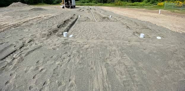 The finished biofilter field covered in sand, with white standpipe caps marking each zone.