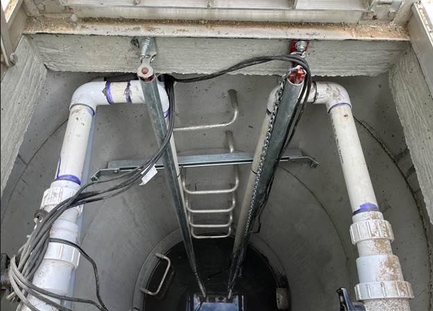 Looking down into the storm water lift station: two discharge pipes, float cables and a ladder in a concrete wet well.