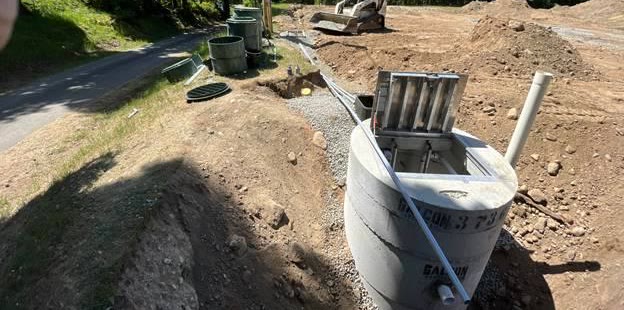 A precast concrete lift station set beside a road, aluminum hatch open, with a track loader working the site behind.