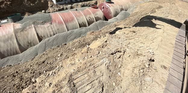 Two long fibreglass septic and pump tanks bedded in gravel in a wide excavation.