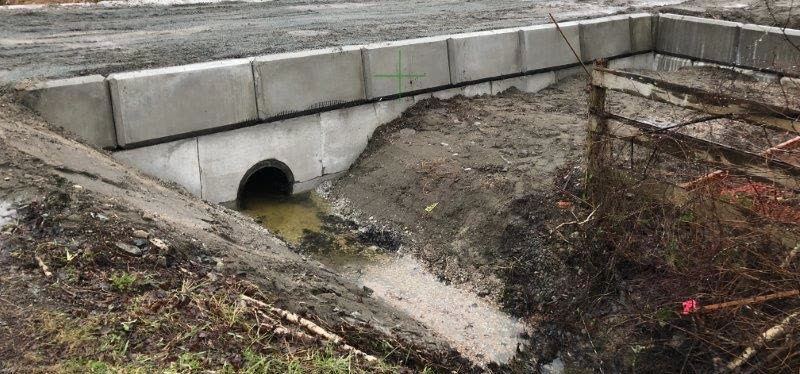 A finished driveway crossing over a ditch: a culvert pipe flowing between two lock block headwalls.