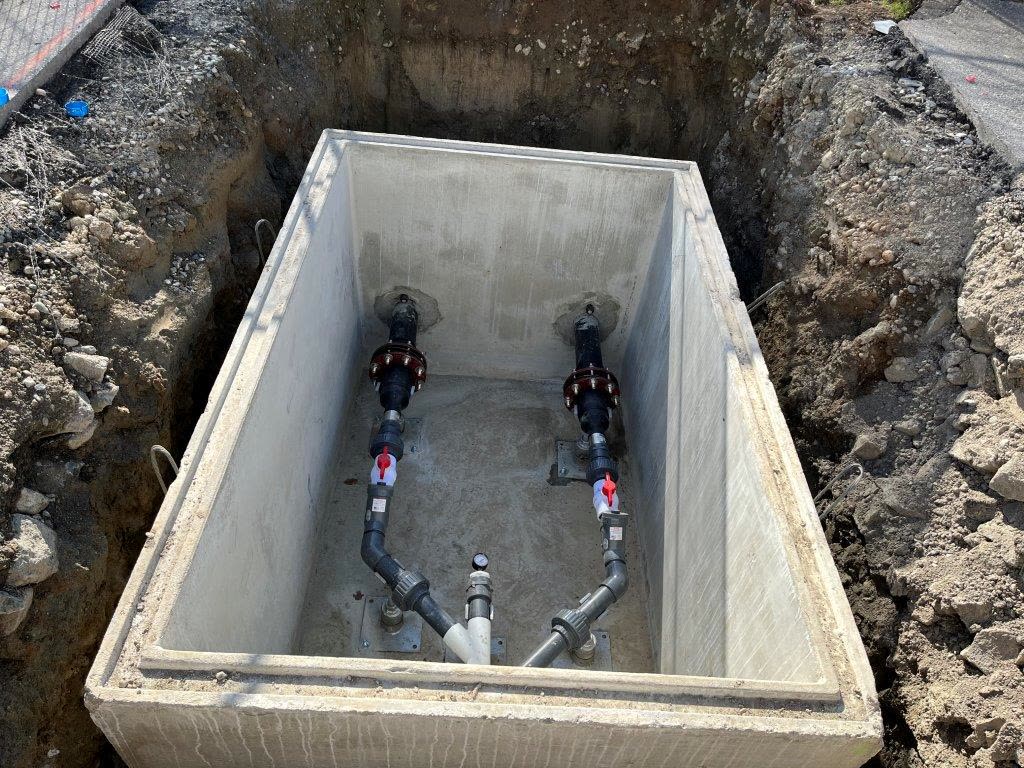 A concrete valve chamber with twin check valves and isolation valves on a commercial lift station.